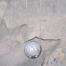 Load image into Gallery viewer, A fitting homage to the elegant and mysterious moon goddess Diana, this medallion style necklace features a weighty and luminous Moonstone cabochon bezel set and ringed with a wide band of solid silver. A sleek chain mounted directly to the edges of the pendant gives a clean finish and keeps the pendant centered.  A 16” chain ensures the pendant will lay comfortably just below your collarbones.