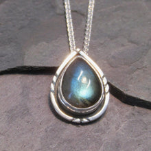 Load image into Gallery viewer, The Labradorite cabochon is absolutely stunning with its deep aqua and teal glow. A rounded offset halo with hand-carved details is oxidized for beautiful contrast. A hidden bail lets the pendant float on the chain with no visual clutter. Subdued enough to class up a t-shirt and jeans but elegant enough to pair with a black dress, this necklace is sure to be a favorite finishing touch!