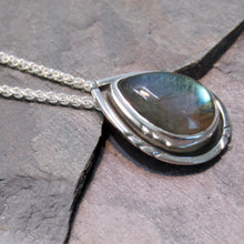 Load image into Gallery viewer, The Labradorite cabochon is absolutely stunning with its deep aqua and teal glow. A rounded offset halo with hand-carved details is oxidized for beautiful contrast. A hidden bail lets the pendant float on the chain with no visual clutter. Subdued enough to class up a t-shirt and jeans but elegant enough to pair with a black dress, this necklace is sure to be a favorite finishing touch!