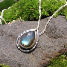 Load image into Gallery viewer, The Labradorite cabochon is absolutely stunning with its deep aqua and teal glow. A rounded offset halo with hand-carved details is oxidized for beautiful contrast. A hidden bail lets the pendant float on the chain with no visual clutter. Subdued enough to class up a t-shirt and jeans but elegant enough to pair with a black dress, this necklace is sure to be a favorite finishing touch!