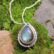 Load image into Gallery viewer, The Labradorite cabochon is absolutely stunning with its deep aqua and teal glow. A rounded offset halo with hand-carved details is oxidized for beautiful contrast. A hidden bail lets the pendant float on the chain with no visual clutter. Subdued enough to class up a t-shirt and jeans but elegant enough to pair with a black dress, this necklace is sure to be a favorite finishing touch!
