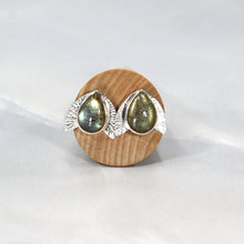 Load image into Gallery viewer, This playful pair of stud earrings features large glowing green Labradorite teardop cabochons flanked by hand-textured silver wings.