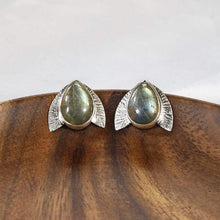 Load image into Gallery viewer, This playful pair of stud earrings features large glowing green Labradorite teardop cabochons flanked by hand-textured silver wings.