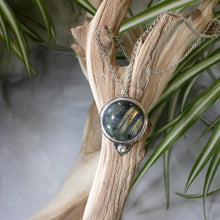 Load image into Gallery viewer, This gorgeous Valarie necklace will be the center of your outfit. A large deep green labradorite with flashy golden stripes is surrounded by a peaked ring of silver and accented by a tiny labradorite set on a hand-textured backer. Delicately hand-cut vine patterns on the back give this piece an extra custom feel.