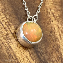 Load image into Gallery viewer, This 9mm Luna necklace features a beautiful orange Ethiopian Opal set simply in a smooth silver bezel. A a diamond cut chain adds a subtle sparkle to complete the clean, classic look you will find yourself wearing over and over.  Details:  Solid sterling silver, partially recycled  Ethiopian Opal  Pendant: 9mm  16” long Sterling Silver chain   Lobster-claw clasp