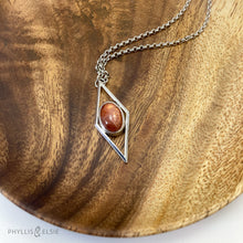 Load image into Gallery viewer, A rich orange oval Sunstone is centered in a diamond frame of polished silver. Beveled edges catch the light and highlight the stone floating in the center.  Details:  Solid sterling silver, partially recycled  Sunstone  Pendant: 17mm x 41mm  18" Sterling chain plus 2" extension   Lobster claw clasp