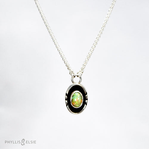 A super flashy Ethiopian Opal wrapped in a silver bezel is framed by a slim patinated shadowbox and hand carved details.   Details  Solid sterling silver, partially recycled  Ethiopian Opal  Pendant: 10mm x 17mm  16” long Sterling Silver chain plus 2
