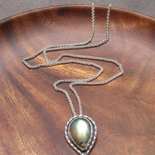 Load image into Gallery viewer, This Stella necklace features a glowing, smooth sage-green Labradorite teardop cabochon that shows glimpses of peach and aqua in bright light. Surrounded with a slightly-offset twisted halo, this pendant stands out despite its small size and soft colors.