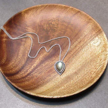 Load image into Gallery viewer, This Stella necklace features a glowing, smooth sage-green Labradorite teardop cabochon that shows glimpses of peach and aqua in bright light. Surrounded with a slightly-offset twisted halo, this pendant stands out despite its small size and soft colors.