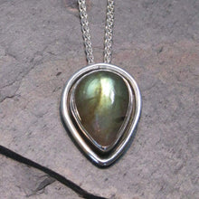 Load image into Gallery viewer, This Stella necklace features an iridescent aqua to amber Labradorite teardop cabochon surrounded by a classic halo of polished round wire. A hidden bail lets the pendant float on the chain with no visual clutter. Simultaneously minimal and unusual, this Stella necklace is the perfect finishing touch to a wide range of looks.