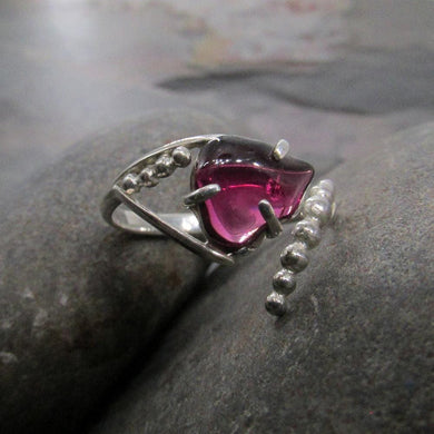 A juicy polished natural Garnet is perched in a .925 Sterling Silver three-prong setting on an asymmetrical ring band studded with silver pebbles. 
