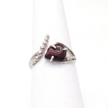 Load image into Gallery viewer, A juicy polished natural Garnet is perched in a .925 Sterling Silver three-prong setting on an asymmetrical ring band studded with silver pebbles. 
