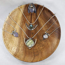 Load image into Gallery viewer, Faye features delicate handcrafted wings to frame this necklace’s substantial eye-catching Green Opal. A beautiful spring green, the stone is striped with shimmering bands and accented by a tiny drop of yellow-green labradorite. Also shown, silver necklaces with moonstone, lilac chalcedony, and labradorite.
