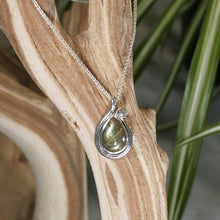 Load image into Gallery viewer, Tara evokes the new life of a seed just sprouted. A green-gold Labradorite is nestled in a tapered silver swirl and topped with a tiny dewdrop Labradorite.

