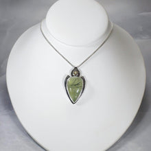 Load image into Gallery viewer, The Jeryn necklace is an absolute showstopper. Featuring a large translucent pear green Prehnite with black tourmaline inclusions, the spearhead shaped pendant is topped off with a luminous peachy green Labradorite set in a hand-texture bezel. A strong and elegant wheat chain balances the piece out and a 2” extension chain allows for neckline options.
