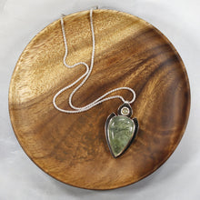 Load image into Gallery viewer, The Jeryn necklace is an absolute showstopper. Featuring a large translucent pear green Prehnite with black tourmaline inclusions, the spearhead shaped pendant is topped off with a luminous peachy green Labradorite set in a hand-texture bezel. A strong and elegant wheat chain balances the piece out and a 2” extension chain allows for neckline options.
