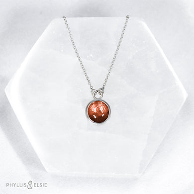 This 10mm Luna necklace features a beautiful rust colored Sunstone set simply in a smooth silver bezel. A slim oval chain completes the clean, classic look you will find yourself wearing over and over.  Details  Solid sterling silver, partially recycled  Sunstone  Pendant: 10mm  16” long Sterling Silver chain   Lobster-claw clasp