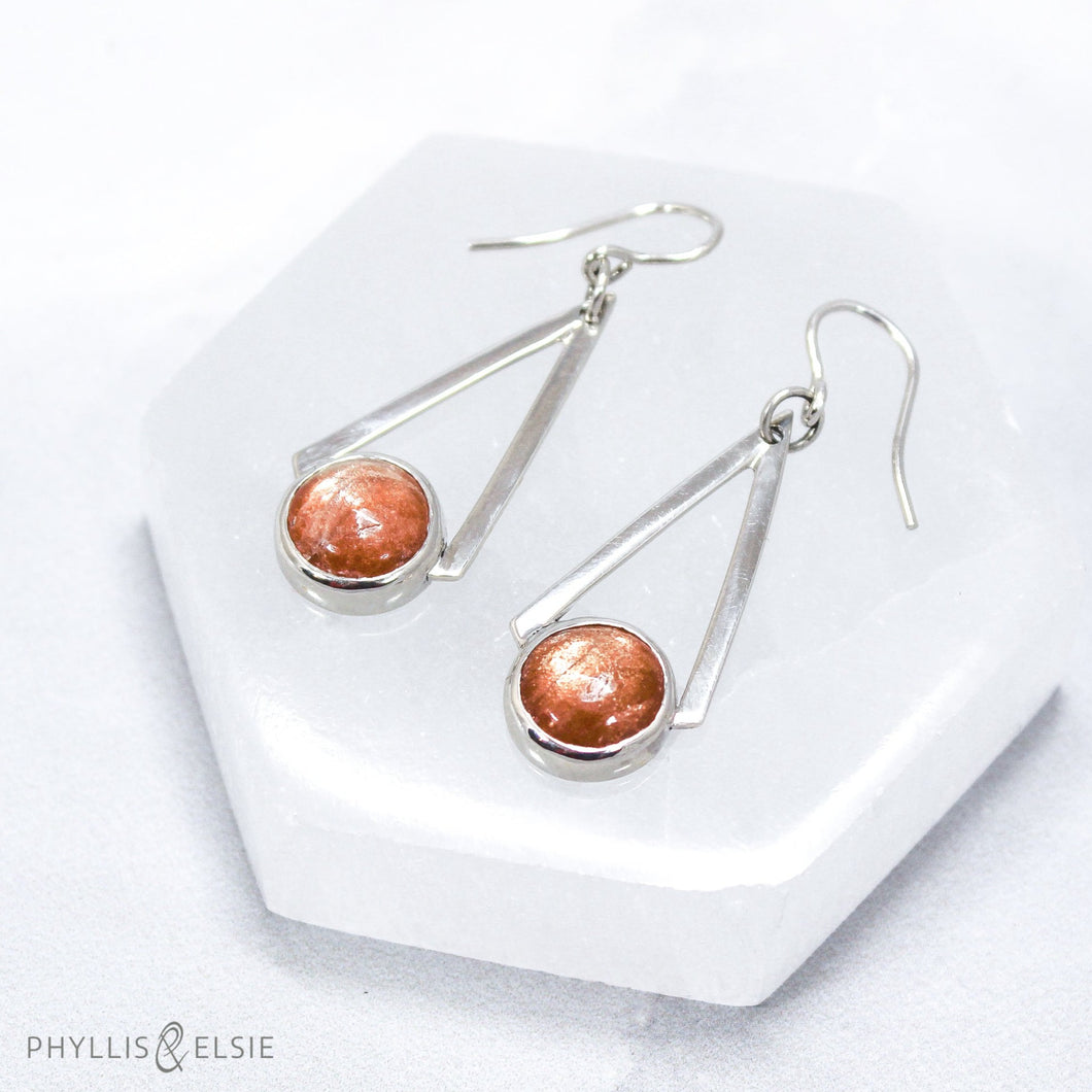 Shimmering Sunstones are suspended between polished silver strips that converge to a point. These bold dangles have all the impact of a big earring without too much weight.  Details  Solid sterling silver, partially recycled  Sunstone  Earring faces: 15mm x 39mm  Sterling ear wires