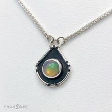 Load image into Gallery viewer, A luminous Ethiopian Opal wrapped in a silver bezel is framed by a geometric shadowbox and hand carved details.   Details:  Solid sterling silver, partially recycled  Ethiopian Opal  Pendant: 14mm x 18mm  16” long Sterling Silver chain plus 2&quot; extension  Lobster-claw clasp
