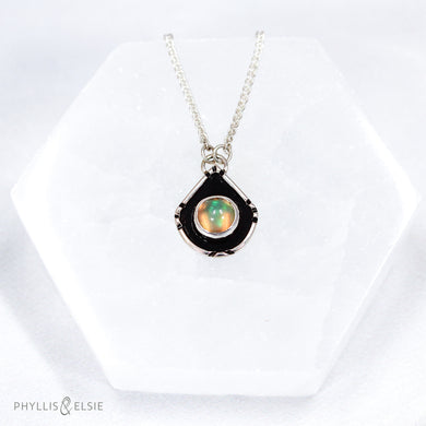 A luminous Ethiopian Opal wrapped in a silver bezel is framed by a geometric shadowbox and hand carved details.   Details:  Solid sterling silver, partially recycled  Ethiopian Opal  Pendant: 14mm x 18mm  16” long Sterling Silver chain plus 2