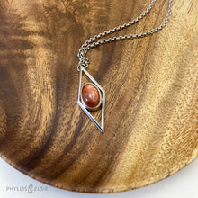 Load image into Gallery viewer, A rich orange oval Sunstone is centered in a diamond frame of polished silver. Beveled edges catch the light and highlight the stone floating in the center.  Details:  Solid sterling silver, partially recycled  Sunstone  Pendant: 17mm x 41mm  18&quot; Sterling chain plus 2&quot; extension   Lobster claw clasp
